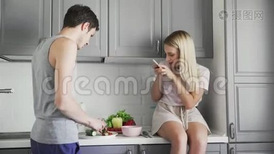 一个女孩给一个在厨房里切蔬菜做沙拉的男人拍照视频