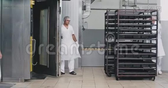 大的面包店里的工人穿着白色制服，把货架上的生面包装在工业烤箱里，以获得烘焙、食品视频