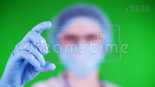 绿色背景。 特写镜头，医生戴着医疗帽、口罩、蓝色医疗手套，手里拿着一张玻璃卡片视频