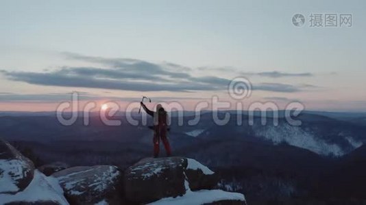 一个孤独的雄性登山者站在山顶上，得意洋洋地举起手来欣赏日落。视频