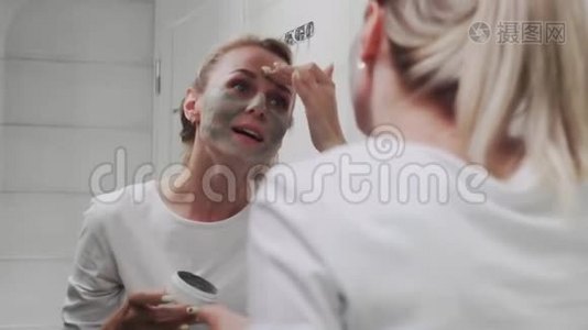一位妇女在镜子前给自己的脸上涂上粘土面膜视频