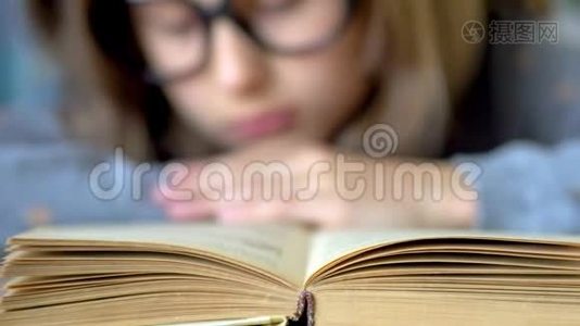 前景是一本书。 一个戴着大黑眼镜的女孩正在看书。 关闭视野。视频