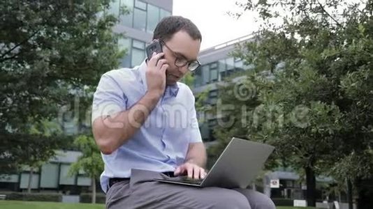 在公园户外工作的商人，使用笔记本电脑和移动电话。视频