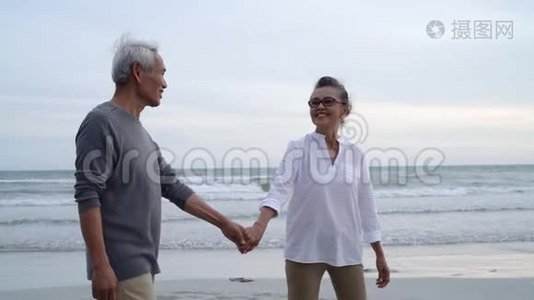 亚洲夫妇老年退休休息放松，手牵手走日落海滩视频