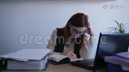 年轻漂亮的工作妇女很累，摘下眼镜，揉着疲惫的眼睛坐在桌上，手提电脑放在桌上视频