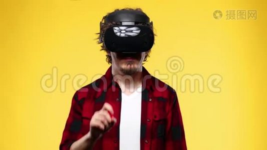 一位留着卷发的年轻人使用VR耳机，在黄色背景下体验虚拟现实视频