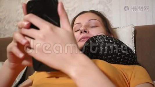 年轻漂亮的白种人女孩早上躺在舒适的卧室里，用智能手机。 笑视频