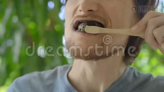 一个绿色环境中的年轻人用黑色活性炭粉刷牙，用于牙齿美白。他用的是视频