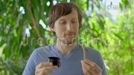 一个绿色环境中的年轻人用黑色活性炭粉刷牙，用于牙齿美白。 他用的是视频