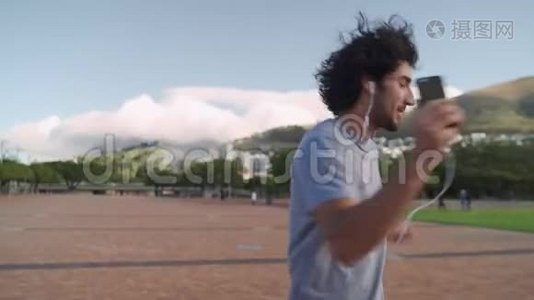 一个年轻的帅哥戴着耳机在公园里随着音乐跳舞视频