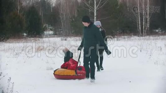 一家人在森林附近的户外跑步和玩耍-男人把他的孩子卷在充气雪橇上视频