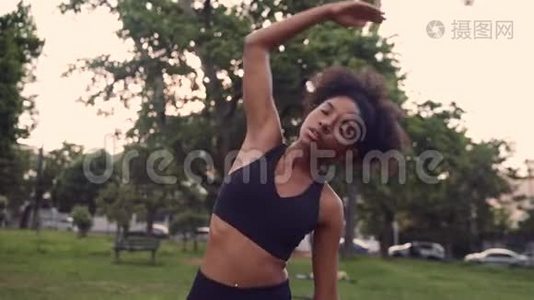 一位健康健康的年轻女性伸展手臂，在公园里热身的肖像。视频