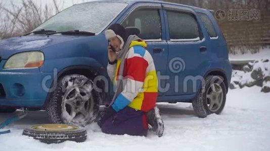 冬天，下着雪。 路上的人汽车出毛病了. 他正试图更换车轮，但他不能`视频