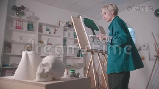 一位年轻的女艺术家在艺术工作室里画画-一个头骨和桌子上的其他人物视频