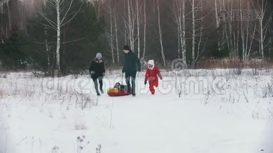 一家人在森林附近的户外玩耍-男人把他的孩子卷在充气雪橇上视频