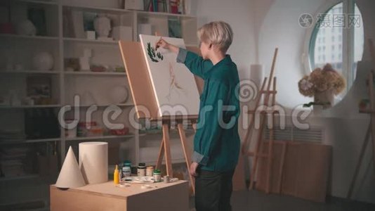一位年轻的金发女艺术家在艺术工作室里用绿色画树上枝视频
