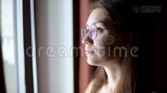 一个戴眼镜的年轻女子望着窗外，期待着来自一个黑暗的房间视频