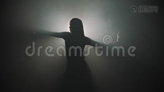 一个年轻迷人的女人的剪影，她的手在明亮的灯光背景下跳舞视频