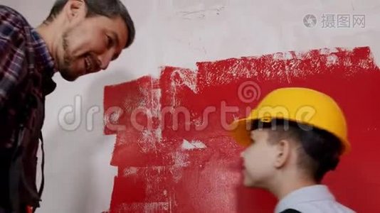 一家人修理一间草稿公寓-小男孩和他的父亲用红色粉刷墙壁视频
