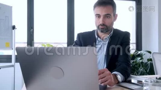 英俊的商人坐在办公室里用笔记本电脑工作。视频