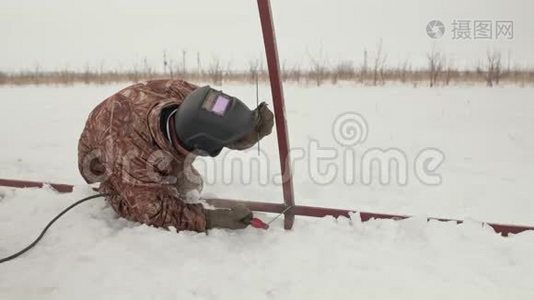 一名专业焊工在雪地里跪着时焊接金属框架。 穿着冬装、手套和电焊面罩的人视频