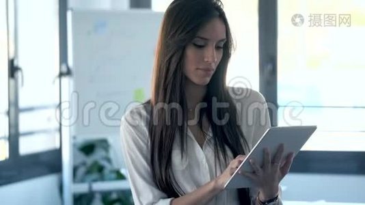 年轻的女商人集中精力使用她的数字平板电脑，同时站在合作空间。视频