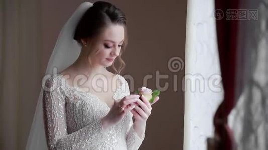 幸福的新娘看着新郎的婚礼，对着窗户微笑。 晨曦从窗户落下视频