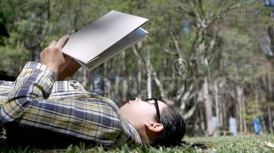 年轻的亚洲女人在度假日在花园里躺在草地上放松和阅读一本书。视频