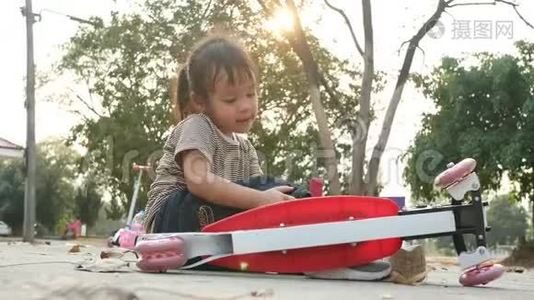 可爱的亚洲小女孩坐在地上后，从她的滑板车在夏季公园。 幼儿健康户外运动..视频