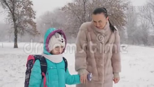 妈妈和小女儿在雪地里牵着手放学回家。视频