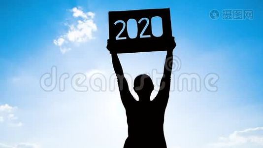 女人拿着回收纸板的剪影，用2020年的文字在蓝天背景和阳光下通过文本。 概念视频