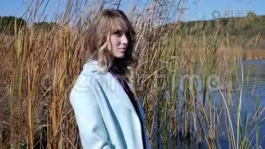 秋天湖上穿着蓝色外套、享受大自然和新鲜空气的年轻女子视频