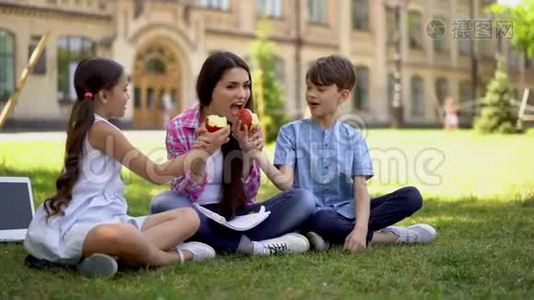 男孩和女孩和坐在户外的自由职业者母亲分享他们的苹果视频