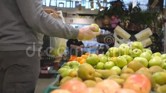 男手在杂货店的生产部门挑选新鲜苹果，并把它放进塑料袋里。 年轻人视频