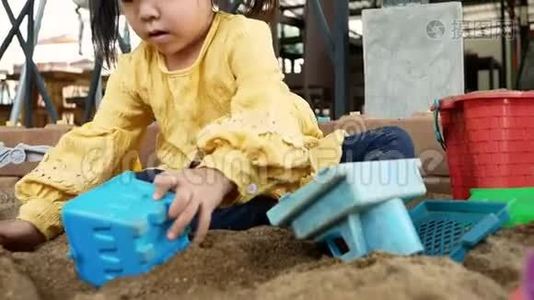 快乐的小女孩在阳光明媚的夏天玩塑料玩具坐在沙箱里。视频