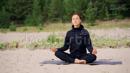 女人坐在沙滩上做瑜伽时正在冥想。视频