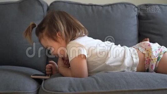 幼儿坐在沙发上，在平板电脑上玩游戏，看动画片.. 现代童年。视频