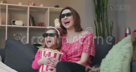 女人和一个小女孩戴着3D眼镜看电视和吃爆米花。 家庭时间和年轻女孩放松视频