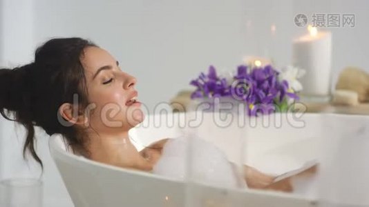 近距离放松的女人在洗澡时吹泡沫。 微笑的女人玩泡沫。视频