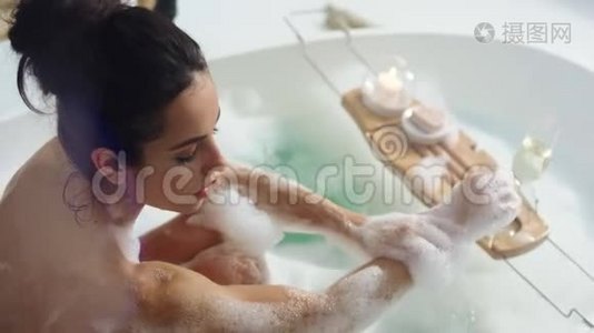 放松的女人用泡沫洗手。 性感女孩在泡沫浴中摸脖子视频