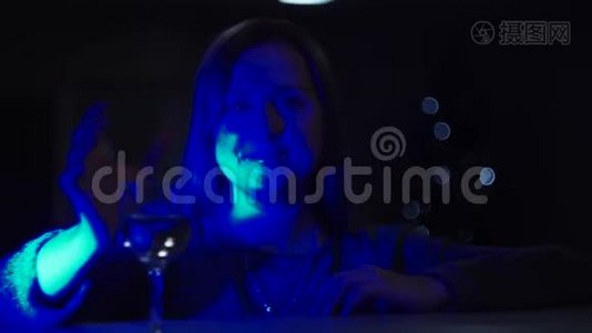 一个女孩在深蓝色的灯光下，有一张耀斑的脸，从杯子里喝葡萄酒视频
