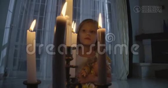 白种人女孩的特写`她的脸在蜡烛后面。 奇怪的孩子拿着洋娃娃环顾四周。 恐惧，恐惧，陌生。视频