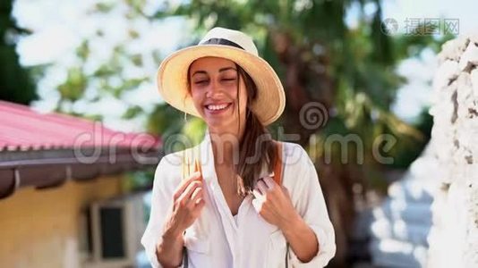 泰国度假时穿着草帽、白衬衫和橙色背包的漂亮女游客走在小街上视频
