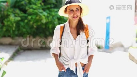 带着草帽、白衬衫和橙色背包的迷人微笑的女游客在老城区的大街上散步视频