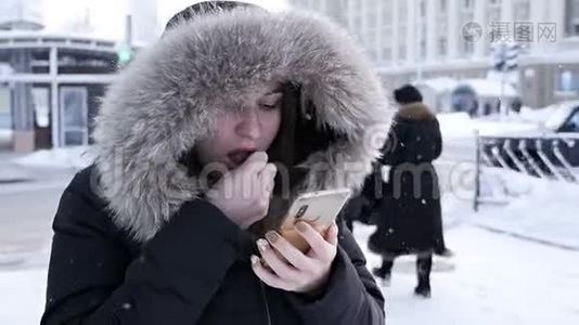 一个女人手里拿着一个电话，想在寒冷的冬天打出租车视频