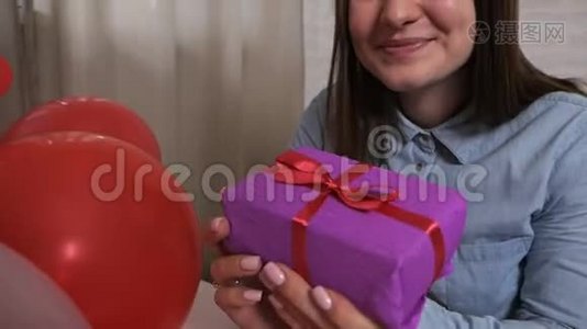 一个微笑的女人拿着一个礼物盒，很高兴，认为那里。 情人节概念视频