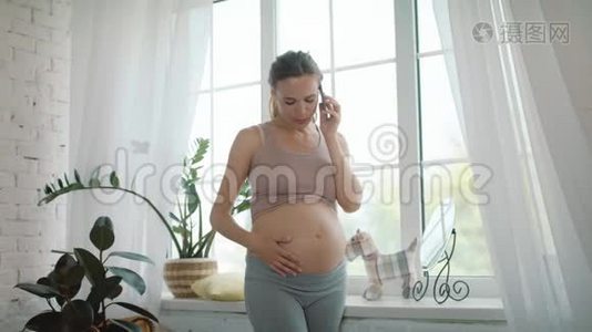 特写微笑孕妇在家轻窗附近通话..视频