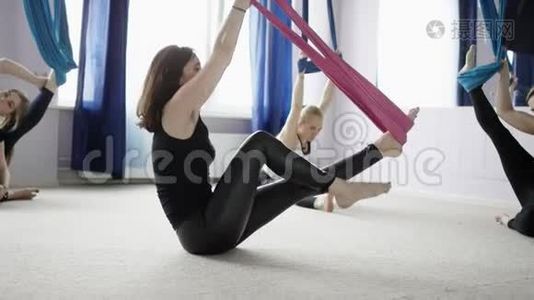 一群年轻的美女在健身俱乐部的紫色吊床上做空中瑜伽练习。视频