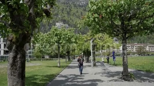 瑞士的一位身穿花纹外套、戴着墨镜的女士在一条绿色公园小巷里漫步视频