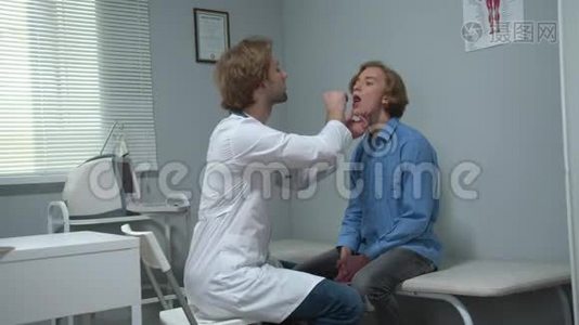 男孩坐在医院的柜子里，医生用棍子检查他的嘴视频